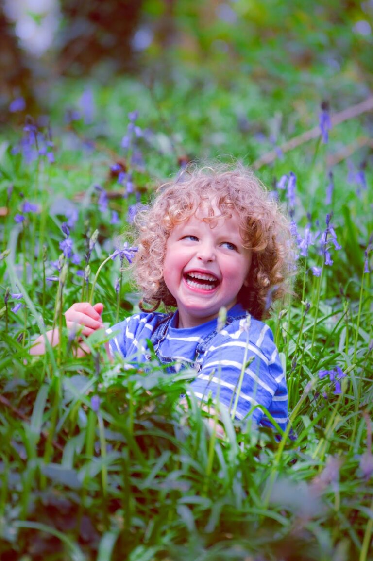 Happy child with blonde curly hair smiling amongst bluebells