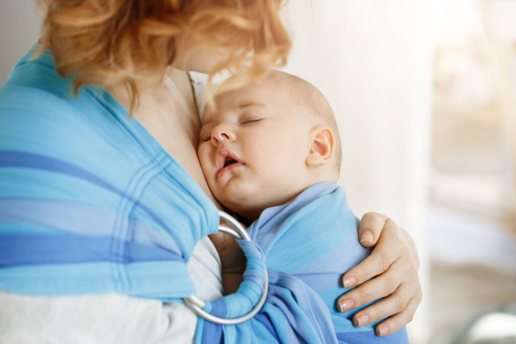 Baby asleep in a blue baby sling on mother's chest