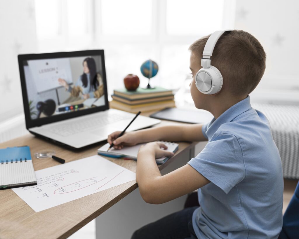 Boy with headphones taking notes during online school