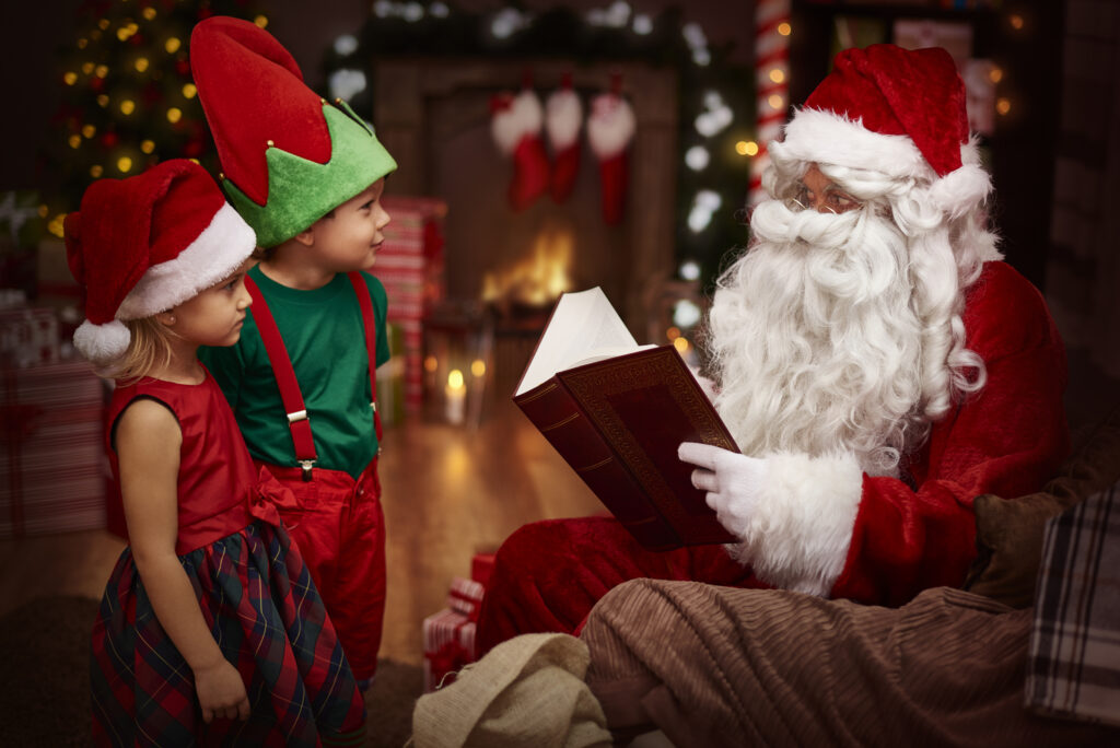 Santa Claus reading a book to children dressed in Christmas outfits